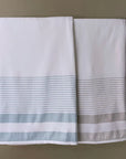 Two white cotton towels with horizontal blue and beige stripes hanging on a beige wall