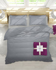 Gray bedding set with a purple blanket on a bed in a bright room.