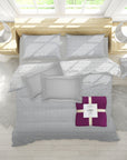 Gray patterned bedding set with a purple blanket on a wooden bed in a bright room.