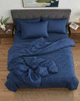 Blue cotton sateen bedding set on a bed in a bedroom with wooden floors and side tables.