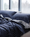 Navy blue and white striped bedding set on a bed with large windows in the background.