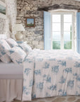 Blue and white toile de Jouy duvet cover set in rustic stone-walled bedroom with window