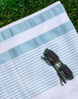 White and teal striped peshtemal towel with sunglasses on grass, beach spa towel