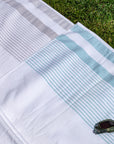 White and teal striped peshtemal towel on grass with sunglasses, spa beach hotel style
