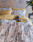 Floral duvet cover set with yellow pillows on a bed, rustic wall, flowers in vase nearby