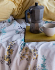 Floral duvet cover with moka pot and cup on bed, yellow pillow in background
