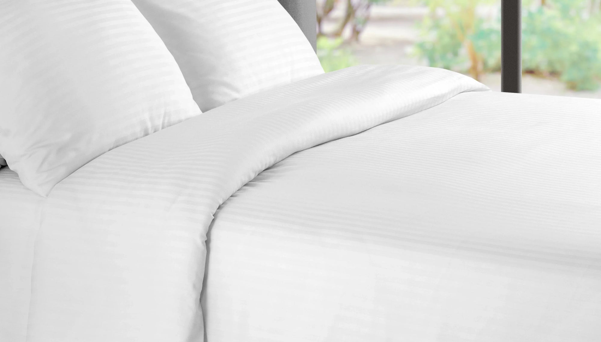 White hotel bedding set with pillows and duvet on a bed near a large window