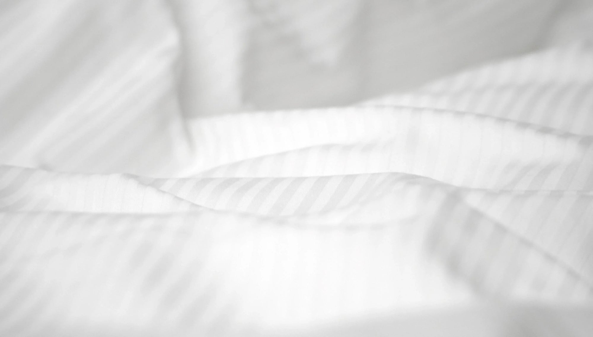 Close-up of white striped cotton bed sheets with soft folds and natural light