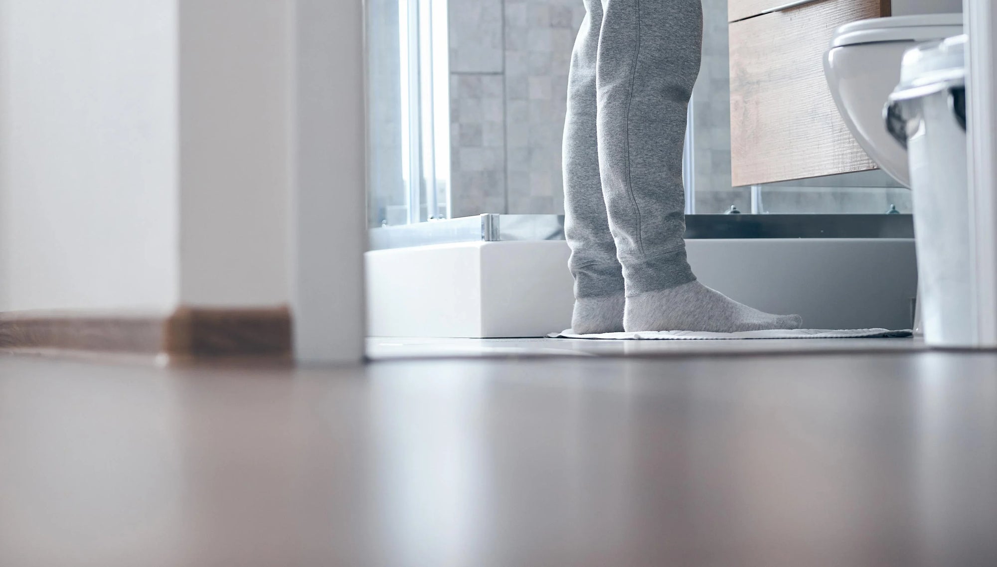 Person in gray sweatpants standing on a white bath mat in a modern bathroom