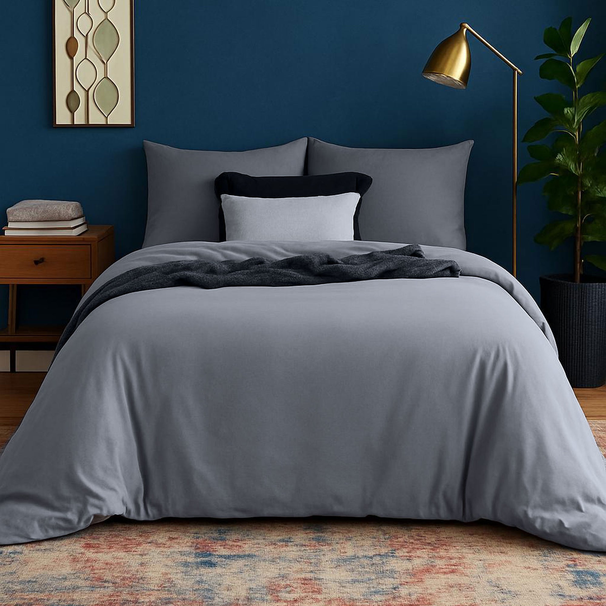Bedroom with gray bedding, nightstand, lamp, and plant against a blue wall.