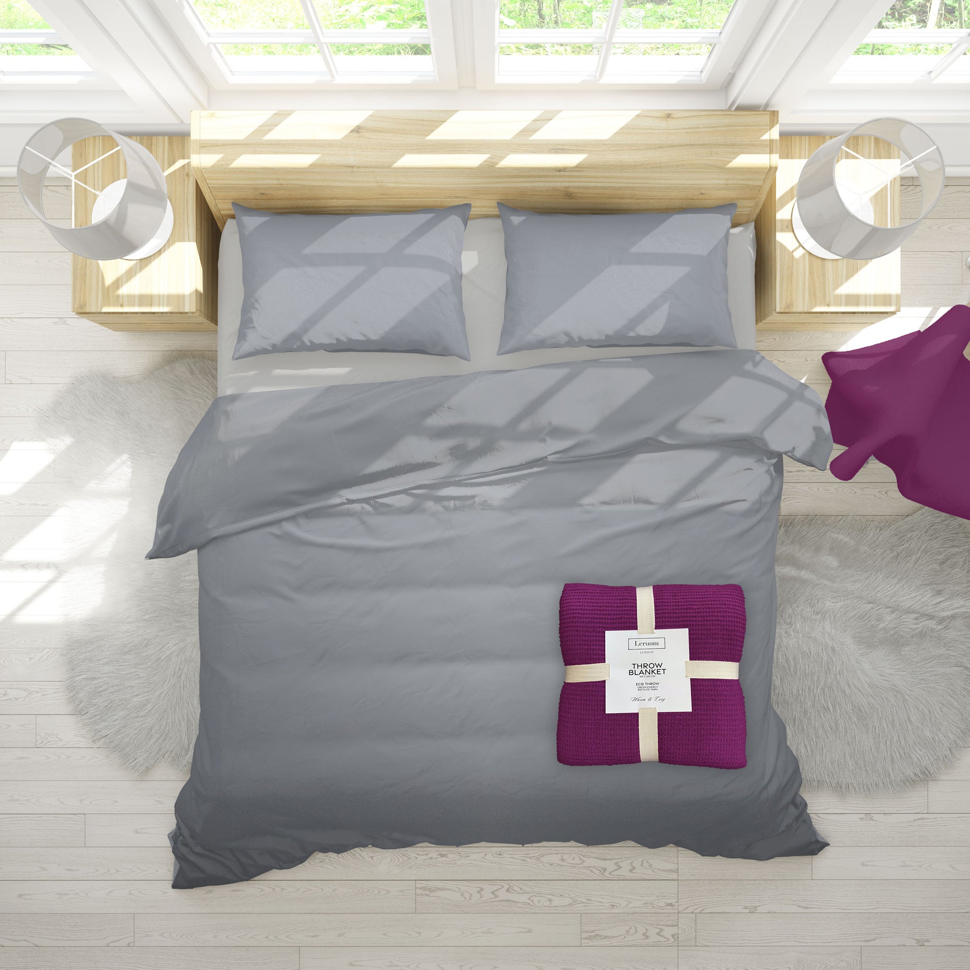 Gray bedding set with a purple blanket on a bed in a bright room.