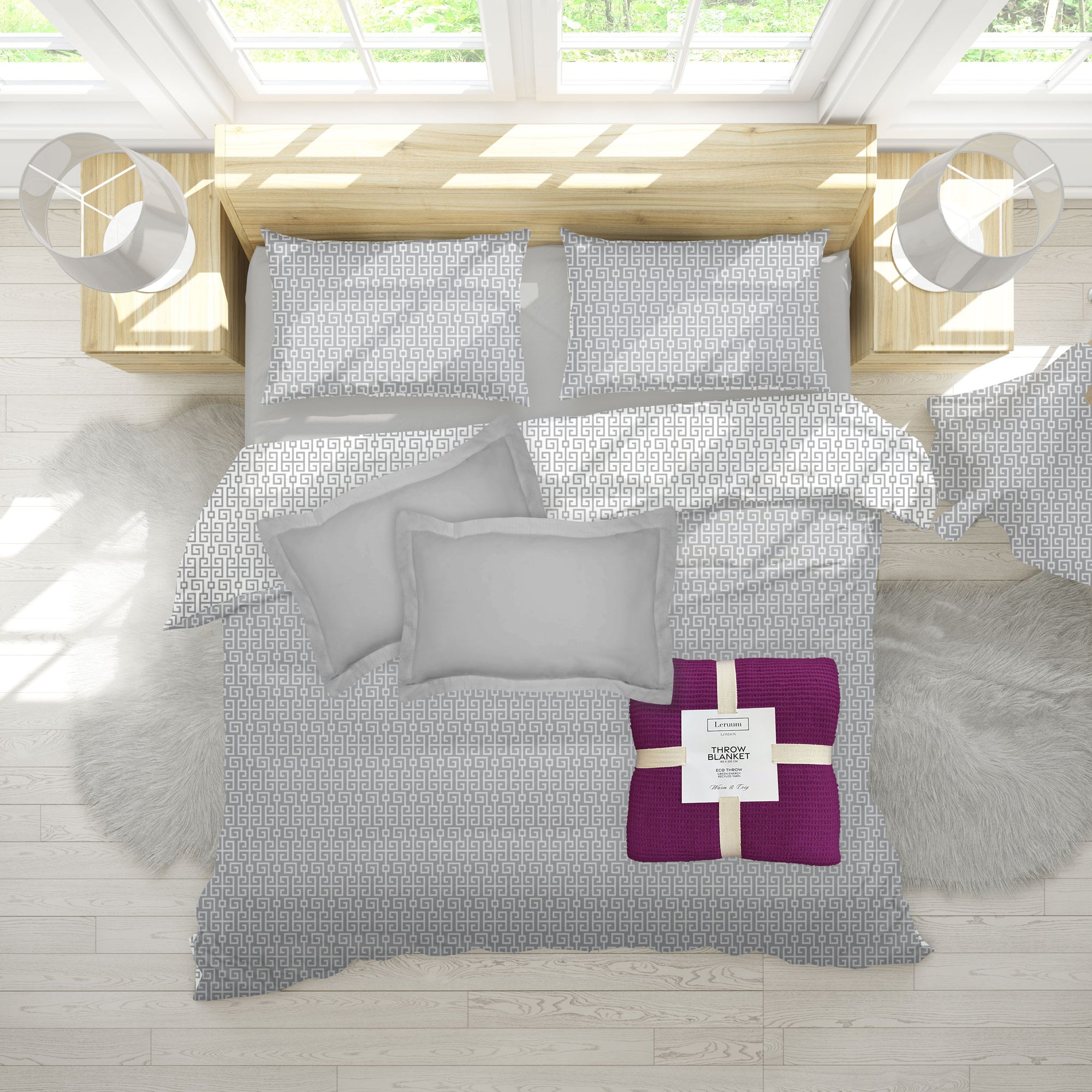 Gray patterned bedding set with a purple blanket on a wooden bed in a bright room.