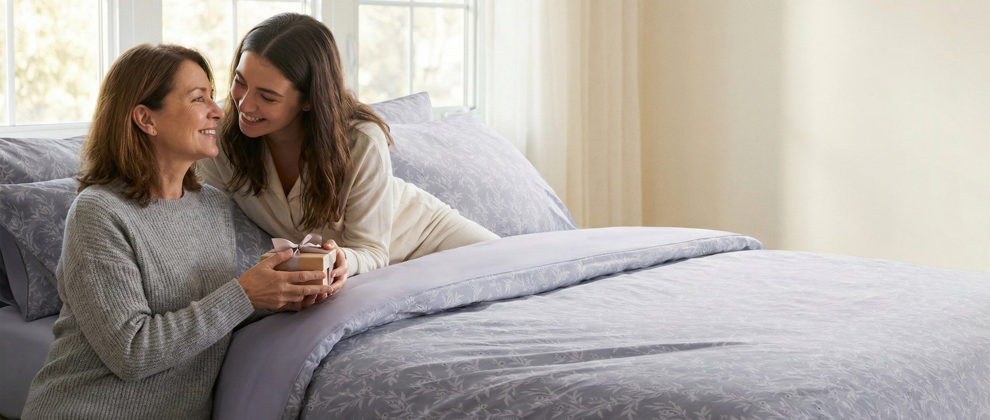 Mother and daughter are sitting on a bed with a pure pewter grey comforter on mothering day UK