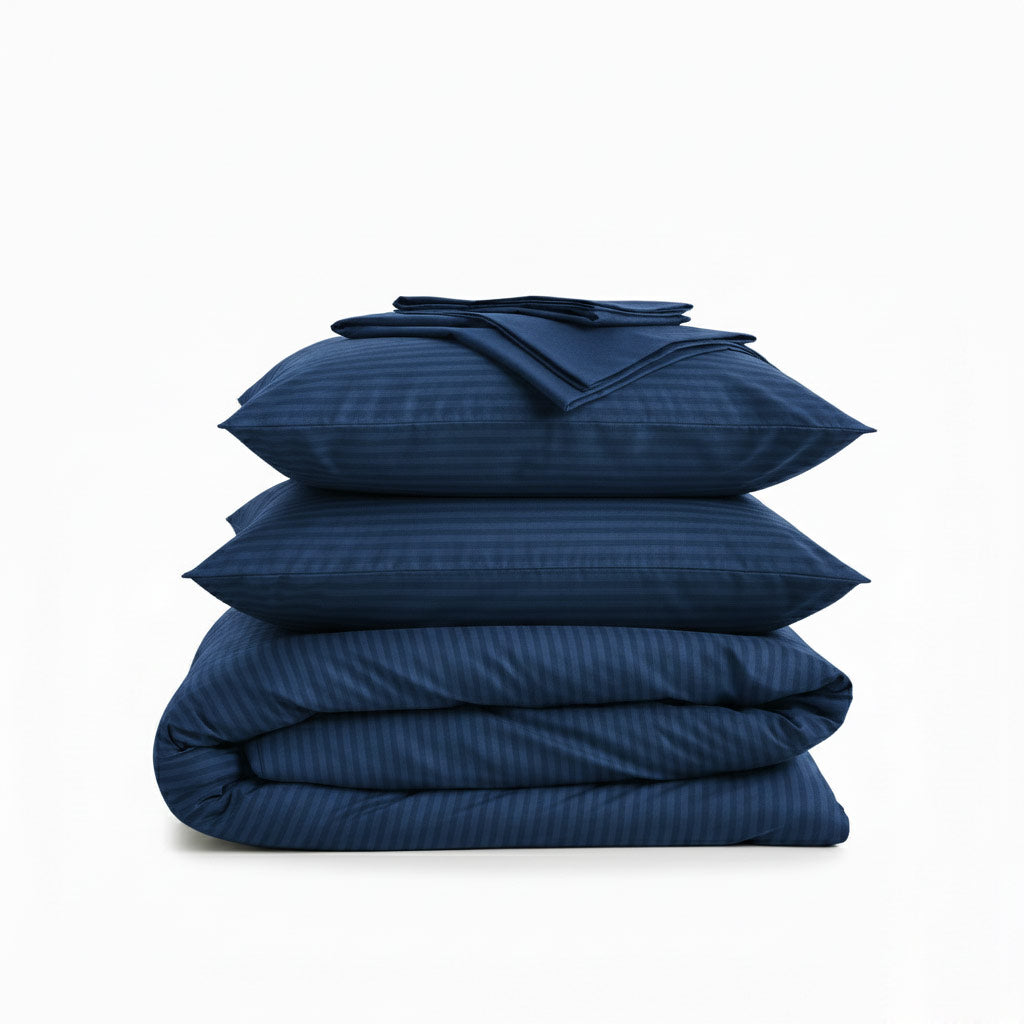 Stack of navy blue cotton sateen bedding bundle including a duvet cover, two pillowcases, and a flat sheet on a white background