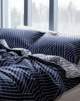 Navy blue and white striped bedding set on a bed with large windows in the background.