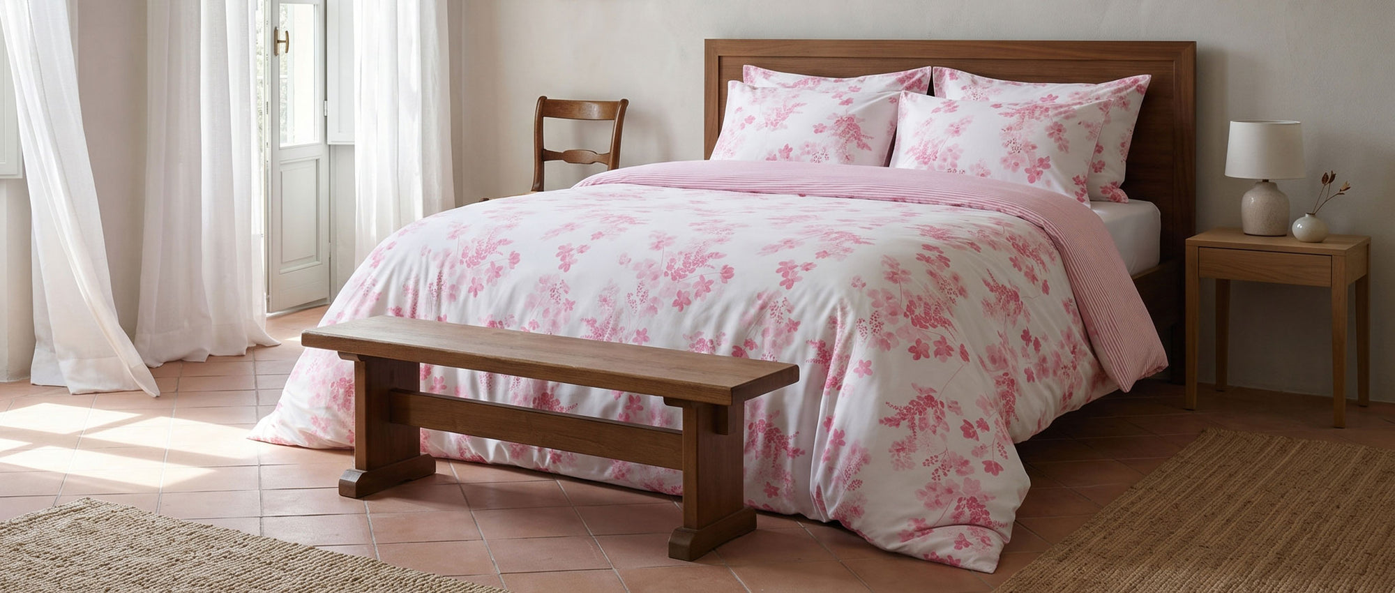 Bedroom with pink floral bedding on a wooden bed, bench, and nightstand.