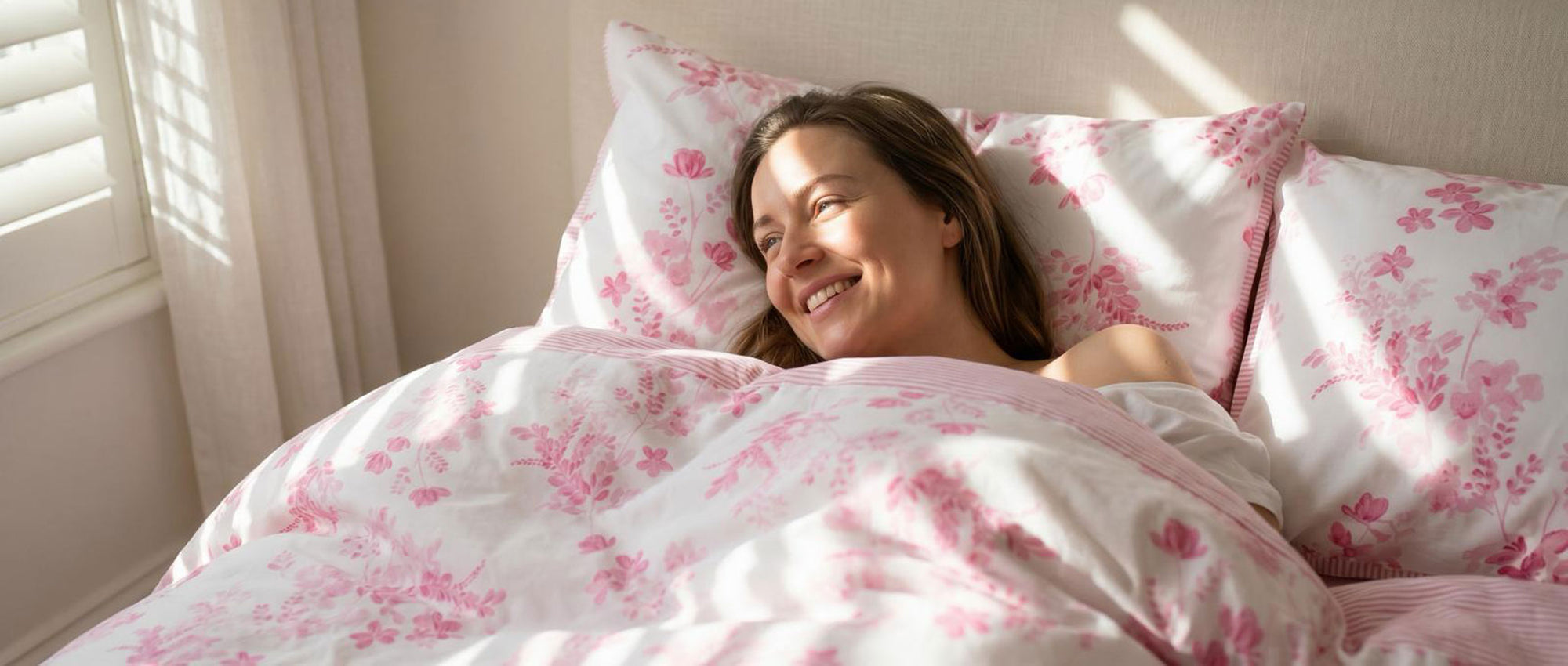 Woman lying in bed with pink floral bedding and pillows.